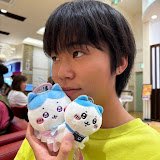 A circular profile photo of a young Japanese woman, Haru, looking to the side while holding two small, blue and white anime plush keychains next to her face.