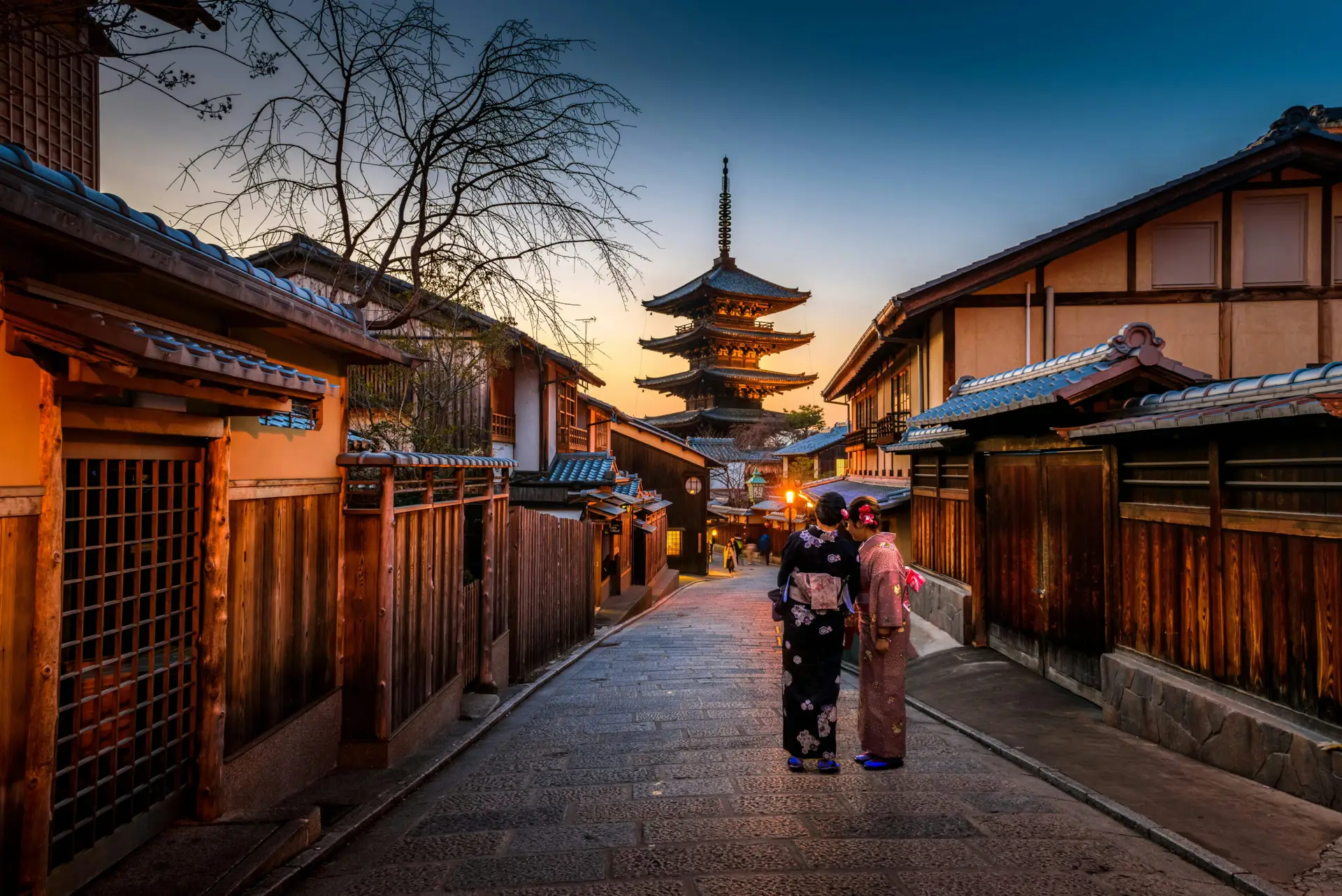 Two women wearing traditional kimono walking through a historic Kyoto street at sunset